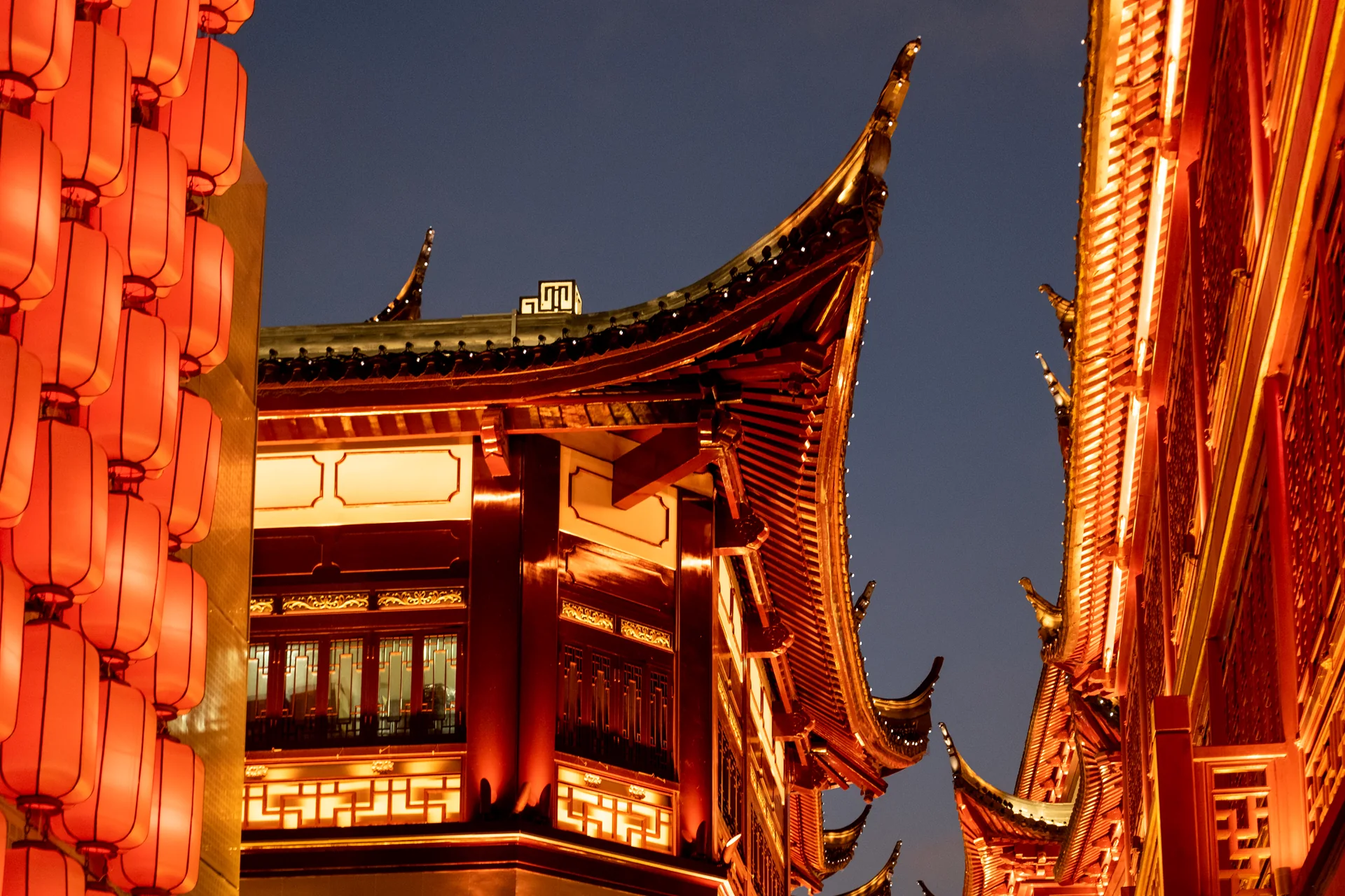 Red lanterns and the lit, upturned eaves of a traditional Chinese building in Shanghai at night