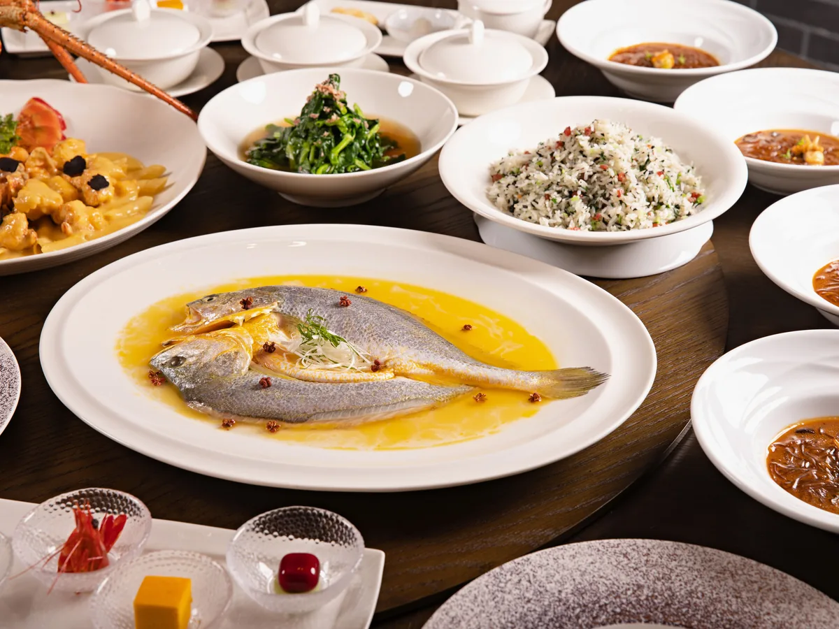 A round banquet table set with multiple Chinese dishes, including a whole steamed fish